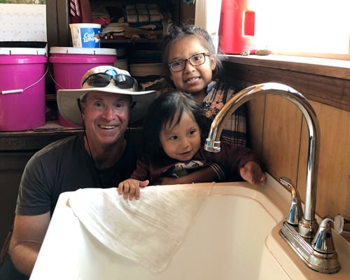 IWSH plumber poses with Navajo children and a new sink